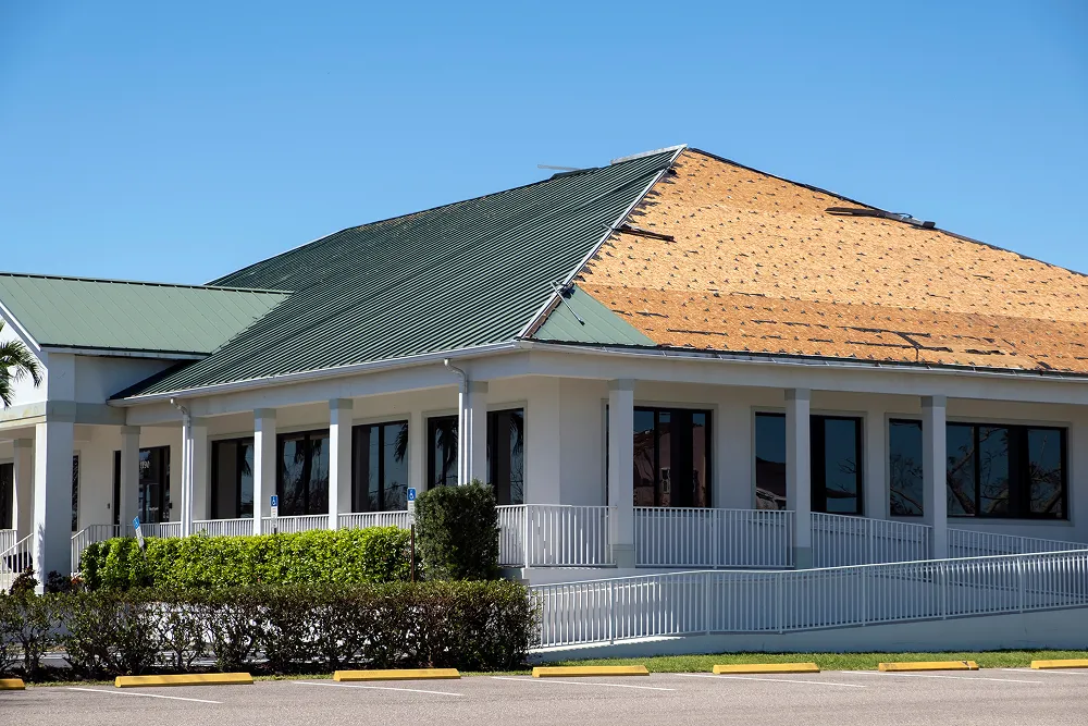 Building with a section of roofing torn away by storm wind, leaving bare sheathing open to the weather